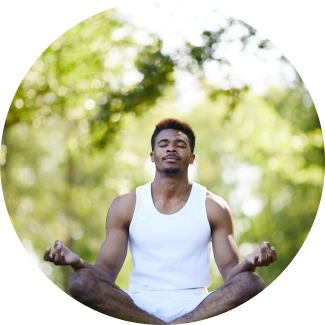 A muscular African man in white vest practicing meditation under a tree