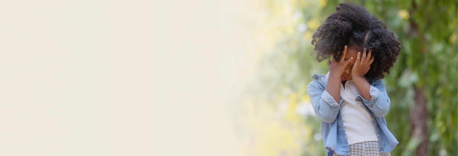 Young participant standing in a open garden with eyes covered with his palm