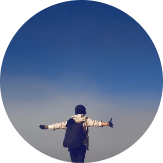 A man standing at a peak with his arms out stretched and taking a deep breath