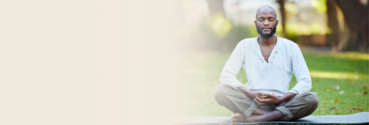 A bearded man practicing meditation on yoga mats in sunny outdoor setting