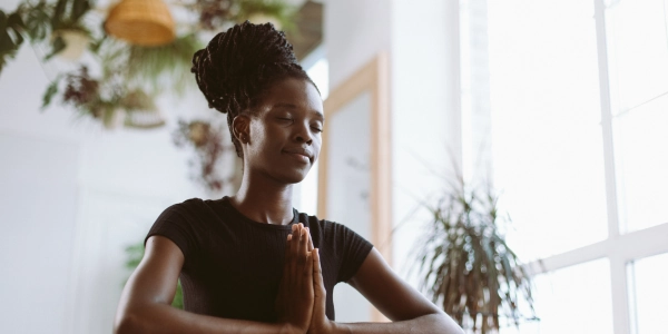 Young African women practicing meditation in a bright room with eyes closed and hands in prayer pose