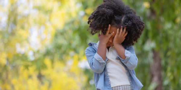 Young participant standing in a open garden with eyes covered with his palm